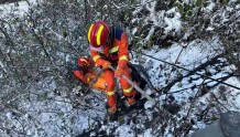 雪天突发车祸1人被困路边悬崖 消防员成功救援